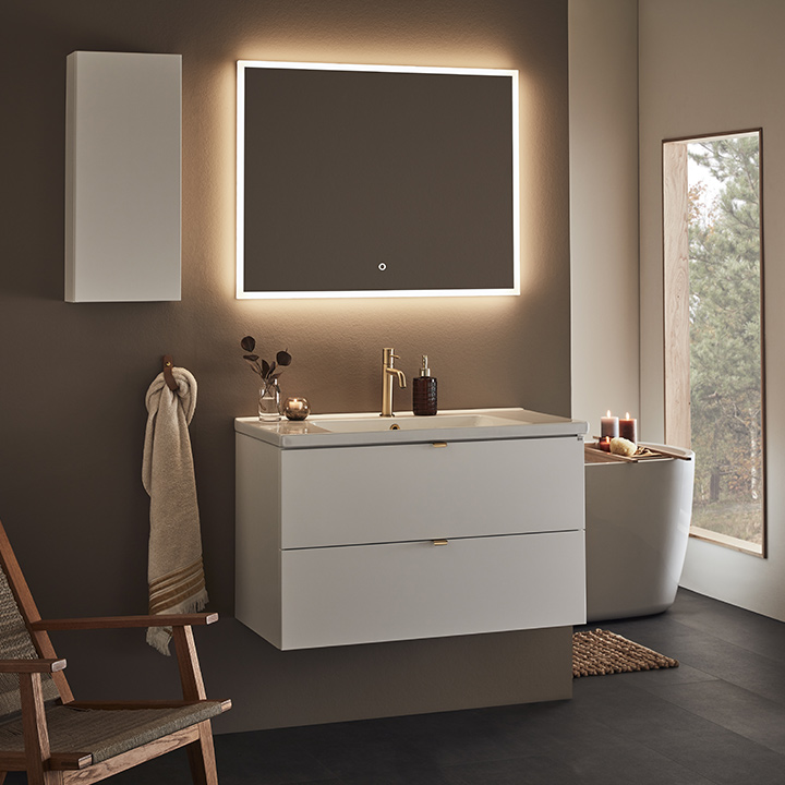 badrumsmöbel vit med mässingsbeslag och porslinstvättställ och spegel med LED